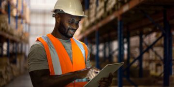 Warehouse worker using digital tablet to check inventory in storage room.