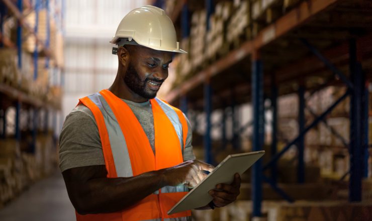 Warehouse worker using digital tablet to check inventory in storage room.